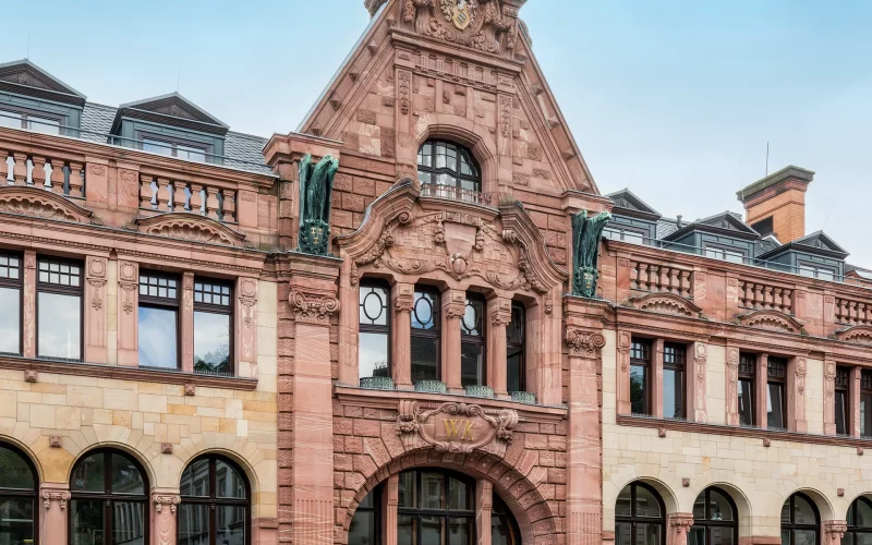 Detailansicht einer repräsentativen historischen Sandsteinfassade mit Rundbogenfenstern, reichem Fassadenschmuck und markantem Mittelgiebel.