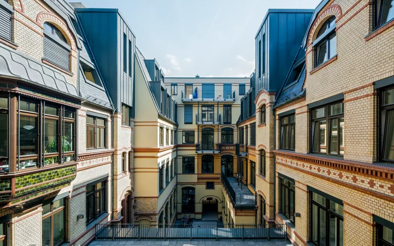 Sanierter Innenhof eines historischen Gebäudekomplexes mit gelben Backsteinfassaden, großen Fenstern und modernen Dachaufbauten.