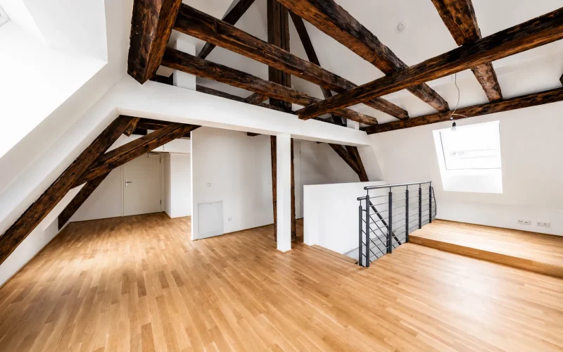 Heller, modernisierter Dachgeschossraum mit Holzboden, sichtbarem Dachgebälk, Dachfenstern und offener Treppe.